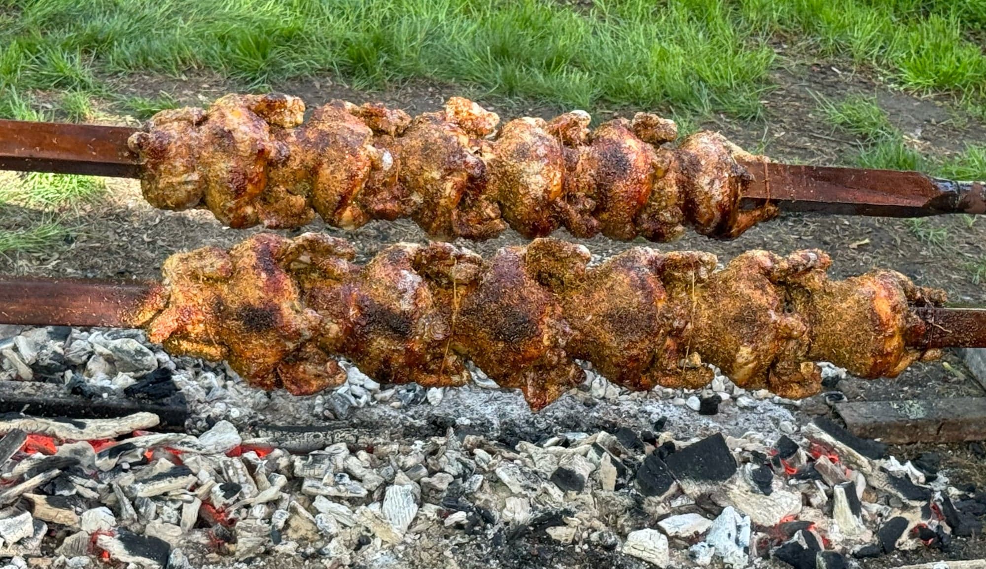 Rows of Greek-style chickens roasting on open spits over charcoal