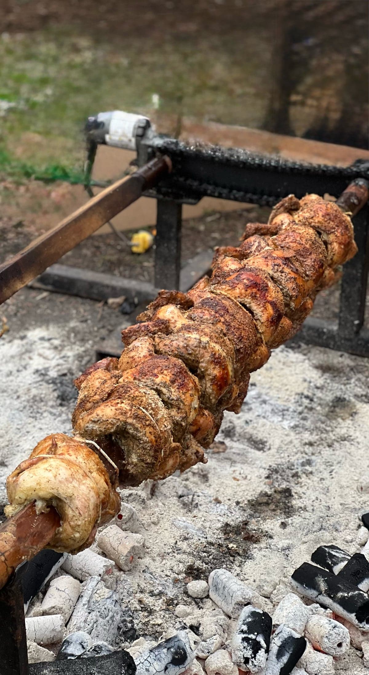 Seasoned whole chickens roasting on an outdoor spit over coals